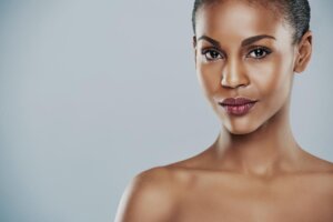 Centered view of beautiful grinning African bare shouldered female with short hair and seductive expression and over gray background