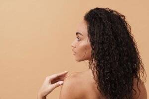 Shirtless black woman with wavy hair posing and looking aside isolated over beige background